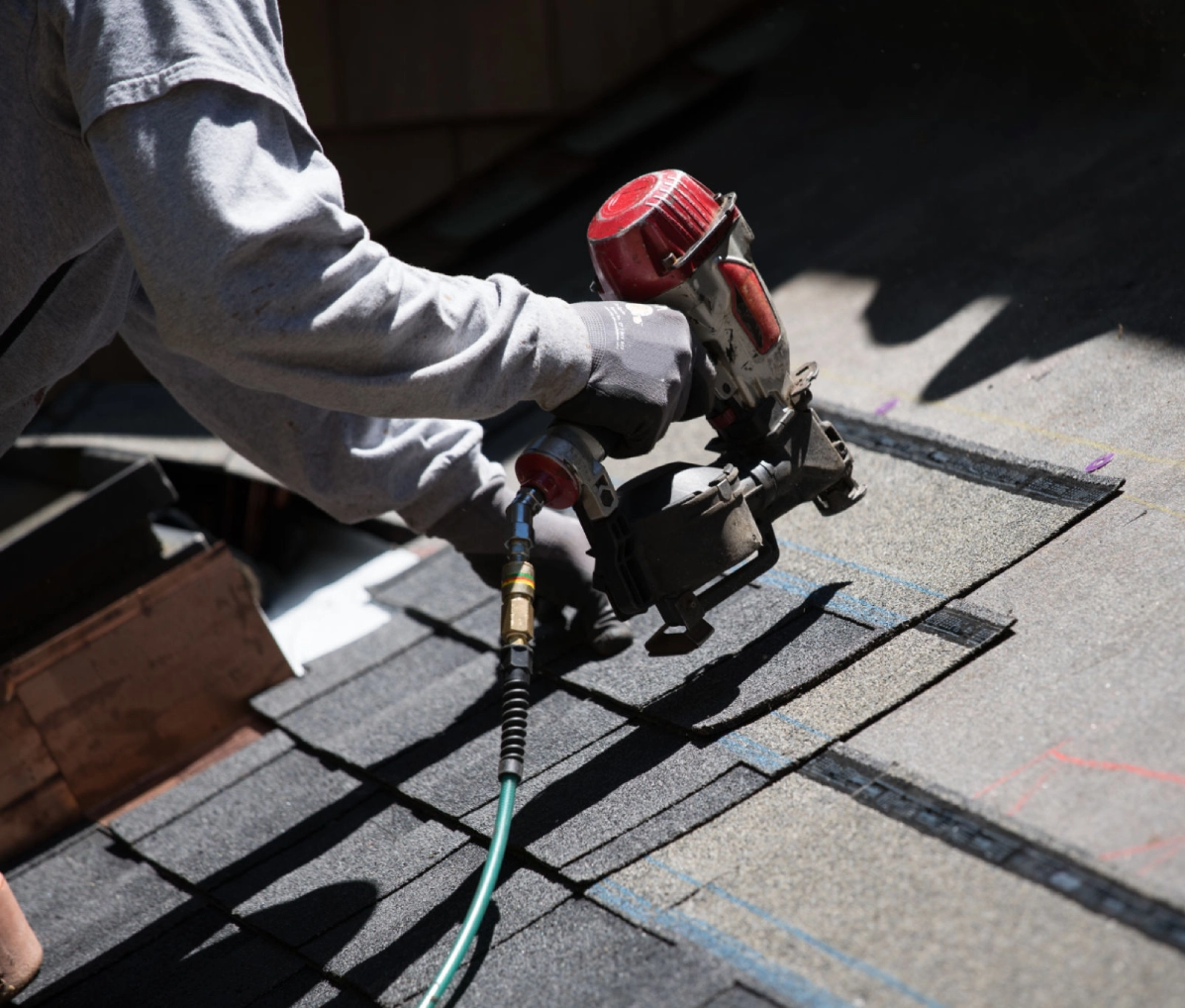 Roofer using nail gun on shingles