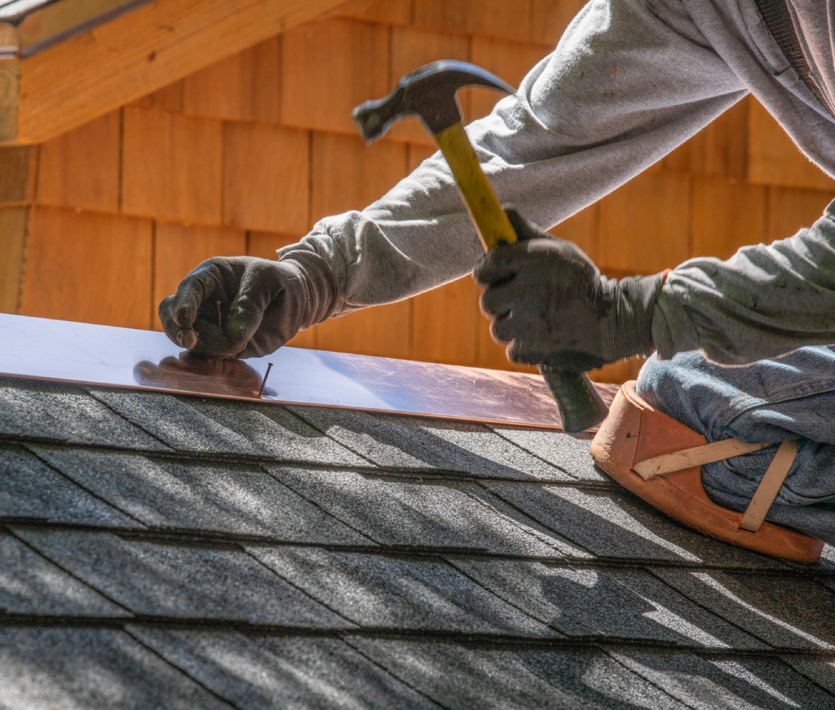 Roofer hammering shingles on roof