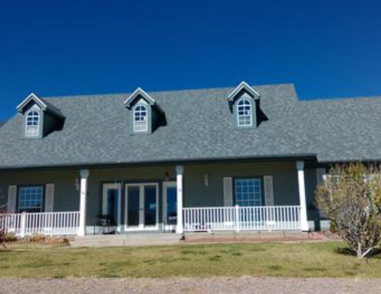 A modern house with a gray roof and a white porch under a clear blue sky.