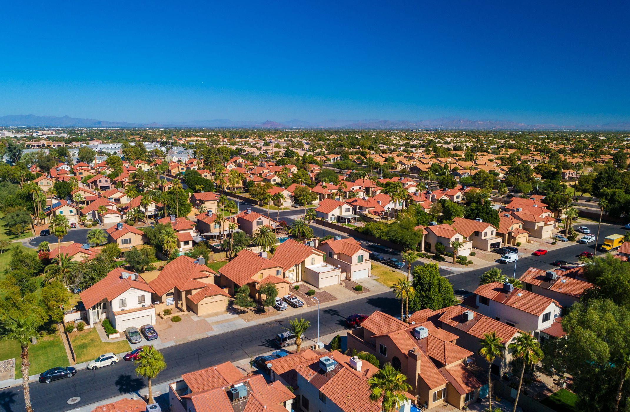 A suburban neighborhood with red-tiled roofs under a clear blue sky.