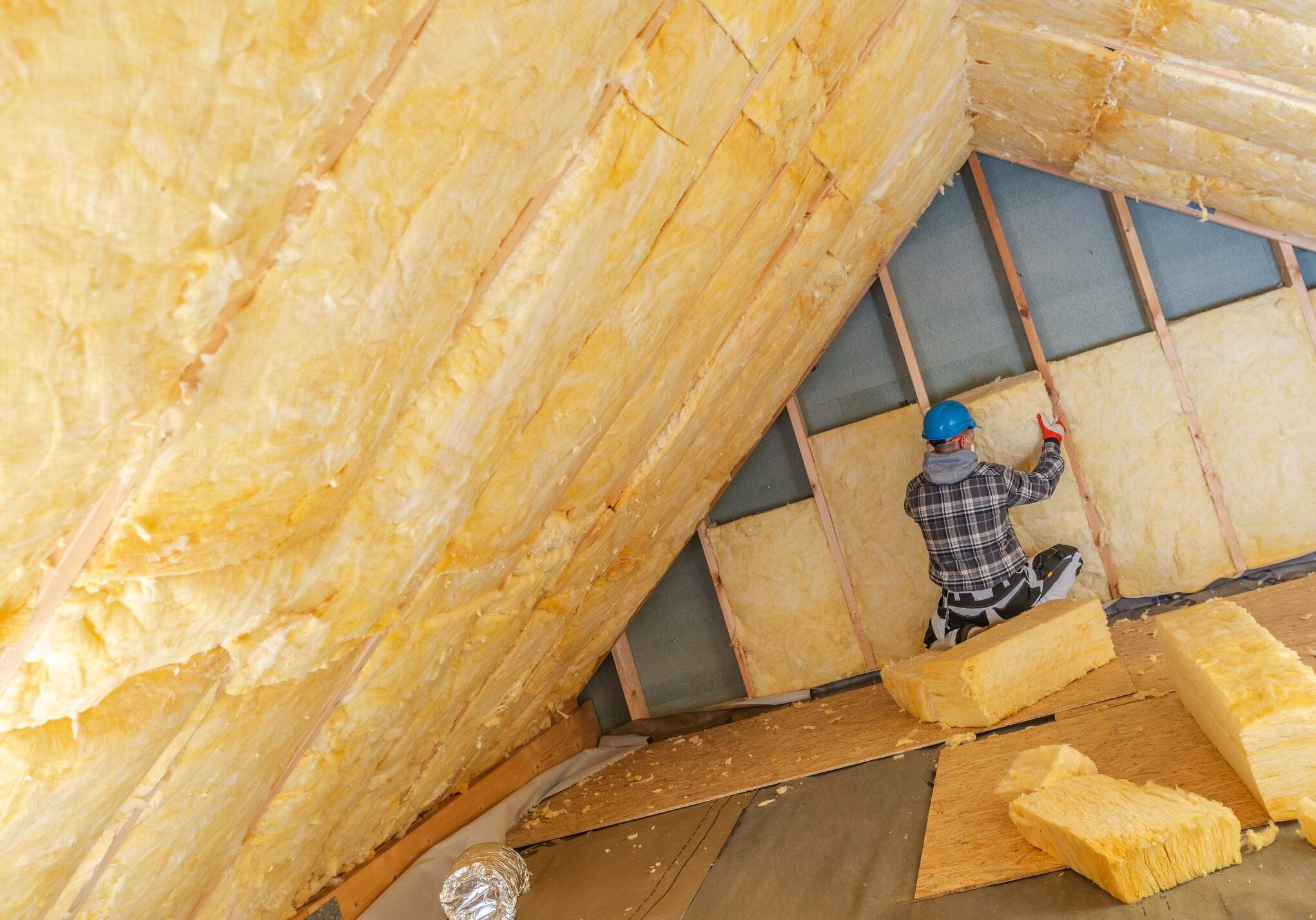 Worker installing yellow insulation foam in an attic space.